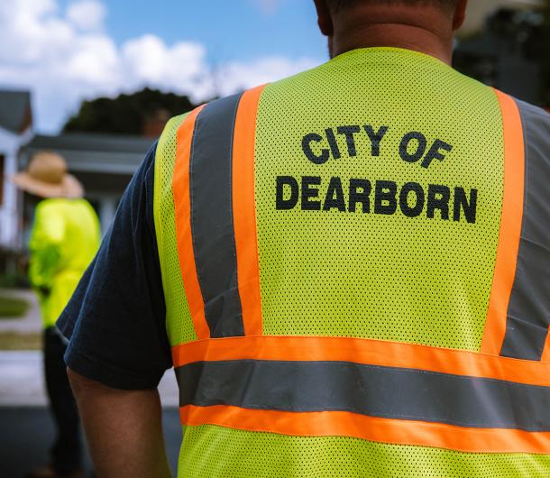 A employee wearing a yellow vest with "City of Dearborn" printed on the back fixes a residential road. 