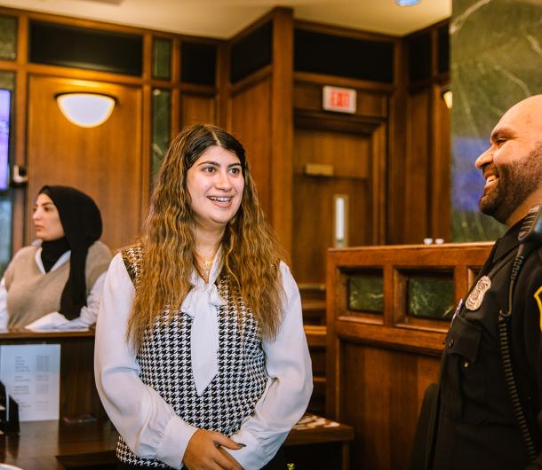 A female member of the 19th District Court staff speaks with a male police officer at the Court. Behind them, a female colleague is seen in a conversation with others. 