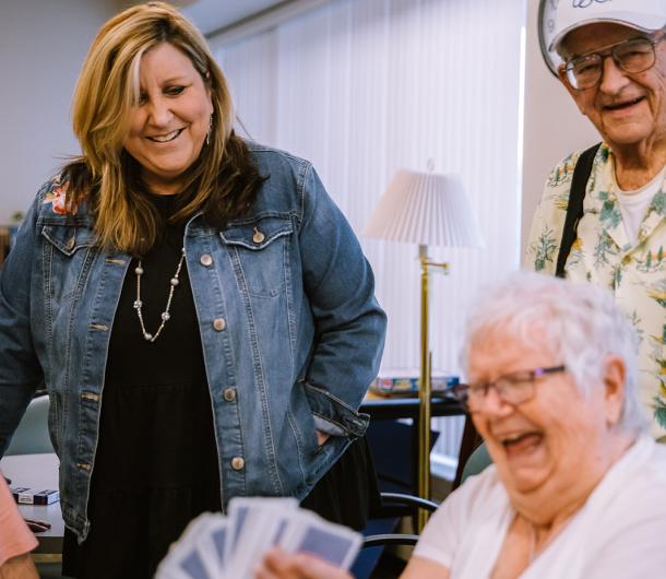 A female member of the Senior Services staff plays cards with two community members. 